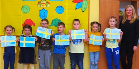 Powiększ grafikę: Obraz przedstawia uczniów i nauczycielkę. Każdy uczeń trzyma odręcznie wykonaną flagę Szwecji.