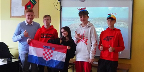 Powiększ grafikę: Obraz przedstawia uczniów trzymających flagę Chorwacji- czterech z nich pokazuje gest uniesionego kciuka. W tle przedstawiony jest krajobraz Chorwacji (morze i wybrzeże).