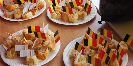 Powiększ grafikę: Obraz przedstawia talerze z potrawami kuchni belgijskiej, w które wbite są wykałaczki z flagą Belgii.