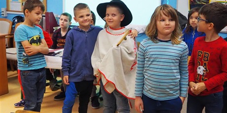 Powiększ grafikę: Obraz przedstawia dzieci stojące w klasie. Jeden z chłopców ma góralskie przebranie (narzutę, kapelusz, ciupagę).