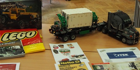 Powiększ grafikę: Obraz przestawia ciężarówkę z klocków lego stojącą na biurku, pudełko lego oraz gazetki sklepów Netto i Jysk.