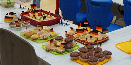 Powiększ grafikę: Obraz przedstawia wypieki stojące na stolikach z wbitymi wykałaczkami z flagami Niemiec.