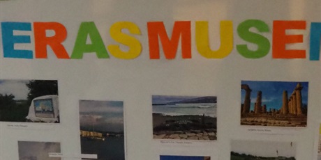Powiększ grafikę: Obraz przestawia tablicę z przyczepionymi zdjęciami przedstawiającymi różne krajobrazy. Na środku jest kolorowy napis „Z Erasmusem +”.