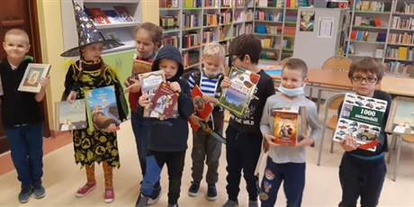 Powiększ grafikę: Zdjęcie przedstawia grupę dzieci, które trzymają w rękach książki. W tle regały z książkami.