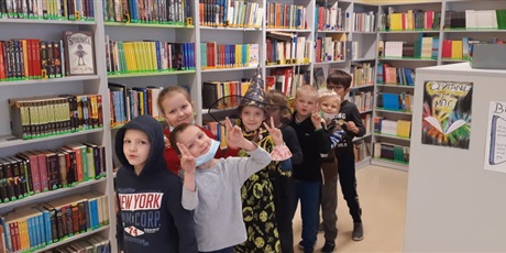Powiększ grafikę: Zdjęcie przedstawia grupę dzieci, które stoją w rzędzie. W tle regały z książkami.