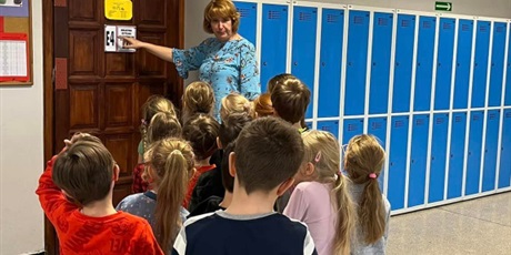 Powiększ grafikę: Na zdjęciu grupa dzieci i nauczycielka stoją na korytarzu szkolnym przed drzwiami biblioteki.